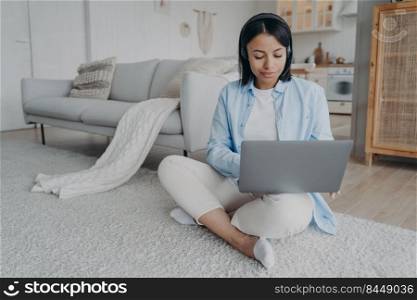 Young arab woman in headset and mic is sitting on floor having video chat on laptop. European girl is smiling and tyπng on pc. Freelancer has∫er≠t session. Student has virtual≤sson.. Young woman is sitting on floor having video chat on laptop. Girl is smiling and tyπng on pc.