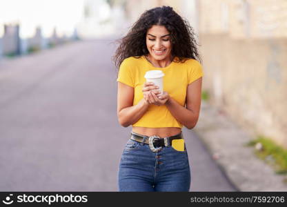 Young Arab woman walking across a urban street with a take-away coffee. Arab girl walking across the street with a take-away coffee