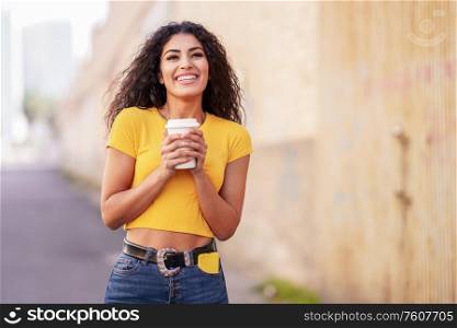 Young Arab woman walking across a urban street with a take-away coffee. Arab girl walking across the street with a take-away coffee