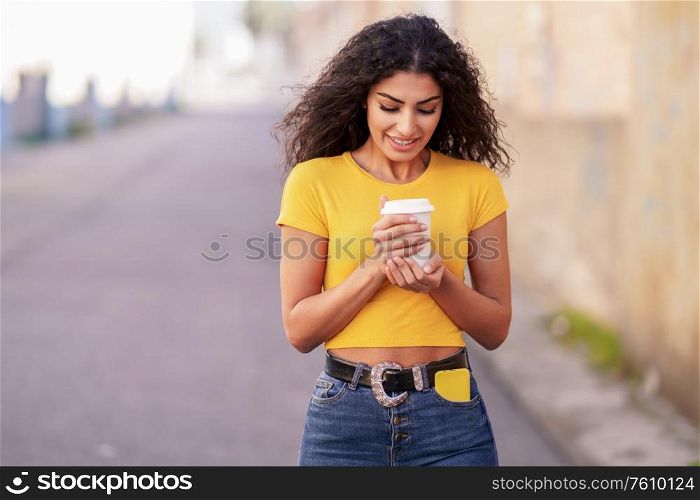 Young Arab woman walking across a urban street with a take-away coffee. Arab girl walking across the street with a take-away coffee