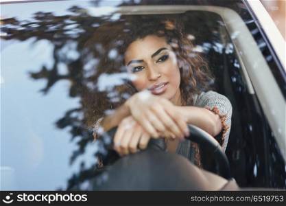 Young arabic woman inside a white car looking through the window. Beautiful young arabic woman inside a nice white car looking through the window. Arab girl wearing casual clothes.