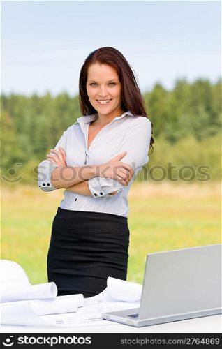 Young architect woman in sunny nature behind table laptop smiling