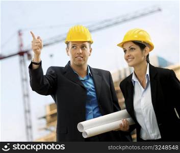 Young architects wearing a protective helmet standing in front of a building site.
