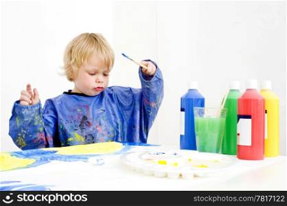 Young artist with a brush in his hands and various bottles of acryllic paint surrounding him