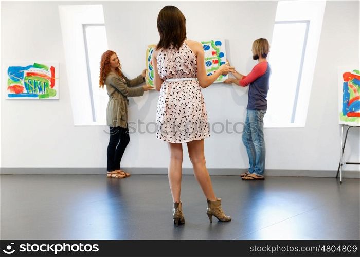 Young artists in gallery hanging painting on walls. Young artists in gallery hanging together painting on walls