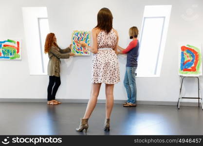 Young artists in gallery hanging painting on walls. Young artists in gallery hanging together painting on walls