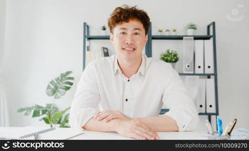 Young Asia businessman using computer laptop talk to colleagues about plan in video call meeting while working from home at living room. Self-isolation, social distancing, quarantine for corona virus.