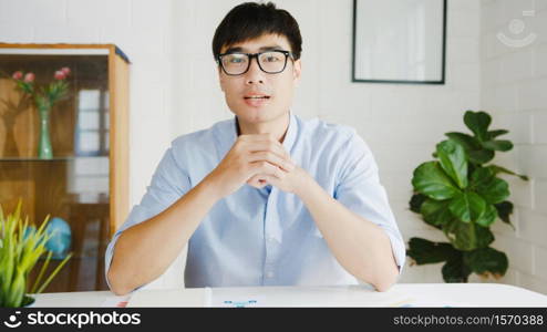 Young Asia businessman using computer laptop talk to colleagues about plan in video call meeting while working from home at living room. Self-isolation, social distancing, quarantine for corona virus.