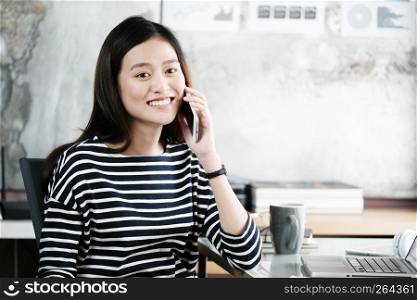 Young asia businesswoman talking smart phone at office desk with happy emotion, working at home, office casual lifestyle concept