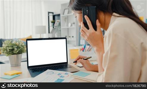 Young Asia businesswoman use smart phone with blank white screen mock up display for advertising text while smart working from home at living room. Chroma key technology, Marketing design concept.