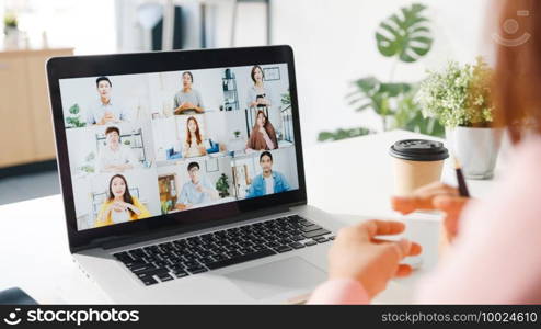 Young Asia businesswoman using laptop talk to colleague about plan in video call meeting while work from home at living room. Self-isolation, social distancing, quarantine for corona virus prevention.