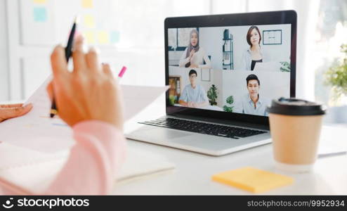 Young Asia businesswoman using laptop talk to colleague about plan in video call meeting while work from home at living room. Self-isolation, social distancing, quarantine for corona virus prevention.