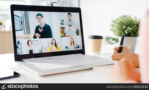 Young Asia businesswoman using laptop talk to colleague about plan in video call meeting while work from home at living room. Self-isolation, social distancing, quarantine for corona virus prevention.