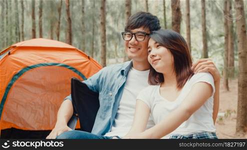 Young asia campers couple sitting in chairs by tent in forest. Male and female traveler relaxing and talking on a summer day at campsite. Outdoor activity, adventure travel, or holiday vacation.