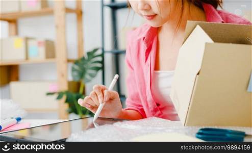 Young Asia entrepreneur businesswoman check product purchase order on stock and save to tablet computer work at home office. Small business owner, online market delivery, lifestyle freelance concept.