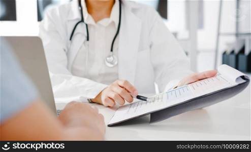 Young Asia female doctor in white medical uniform using clipboard is delivering great news talk discuss results or symptoms with male patient sitting at desk in health clinic or hospital office.