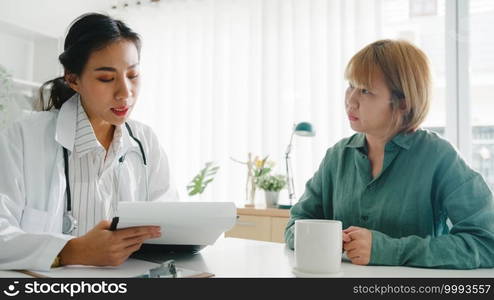 Young Asia female doctor in white medical uniform using clipboard is delivering great news talk discuss results or symptoms with girl patient sitting at desk in health clinic or hospital office.