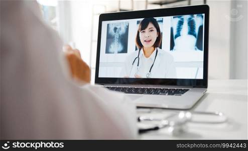 Young Asia female doctor in white medical uniform using laptop talking video conference call with senior doctor at desk in health clinic or hospital. Social distancing, quarantine for corona virus.