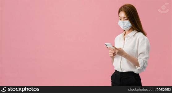 Young Asia girl wear medical face mask use mobile phone with dressed in casual cloth. Self-isolation, social distancing, quarantine for corona virus. Panoramic banner pink background with copy space.