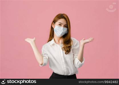 Young Asia girl wearing medical face mask showing peace sign, encourage with dressed in casual cloth and looking at camera isolated on pink background. Social distancing, quarantine for corona virus.