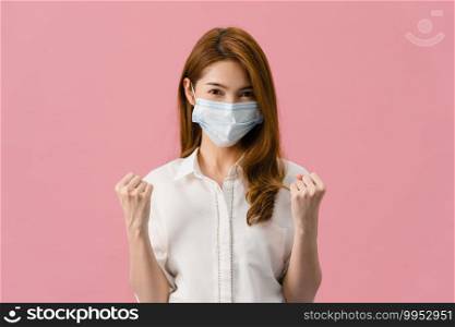 Young Asia girl wearing medical face mask showing peace sign, encourage with dressed in casual cloth and looking at camera isolated on pink background. Social distancing, quarantine for corona virus.