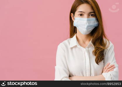 Young Asia girl wearing medical face mask with arms crossed, dressed in casual cloth and looking at camera isolated on blue background. Self-isolation, social distancing, quarantine for corona virus.