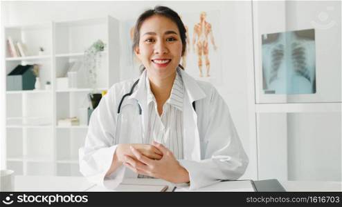 Young Asia lady doctor in white medical uniform with stethoscope using computer laptop talk video conference call with patient, looking at camera in health hospital. Consulting and therapy concept.