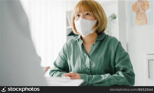 Young Asia lady doctor wear protective mask using clipboard is delivering great news talk discuss results or symptoms with girl patient in hospital office. Lifestyle new normal after corona virus.
