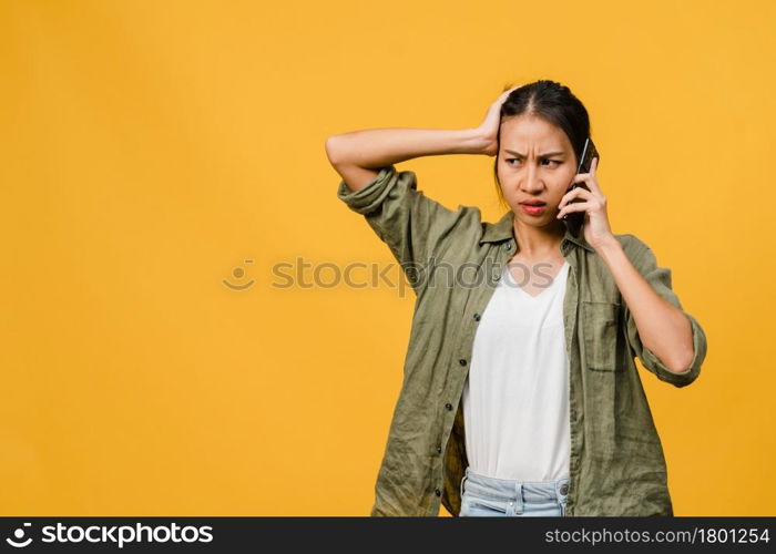 Young Asia lady talk by phone with negative expression, excited screaming, cry emotional angry in casual cloth and stand isolated on yellow background with blank copy space. Facial expression concept.