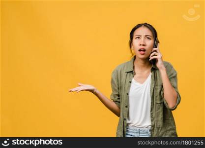 Young Asia lady talk by phone with negative expression, excited screaming, cry emotional angry in casual cloth and stand isolated on yellow background with blank copy space. Facial expression concept.