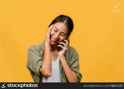 Young Asia lady talk by phone with positive expression, smile broadly, dressed in casual clothing feeling happiness and stand isolated on yellow background. Happy adorable glad woman rejoices success.