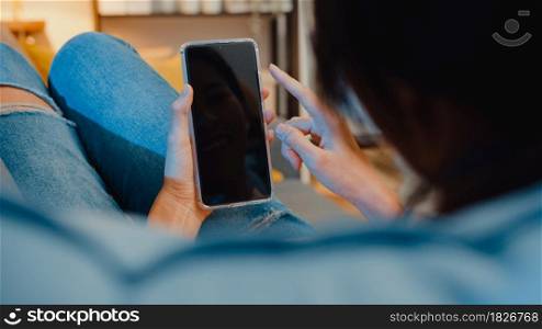Young Asia lady use smart phone with blank black screen mock up display for advertising text while rest on couch in living room at modern home night. Chroma key technology, Marketing design concept.