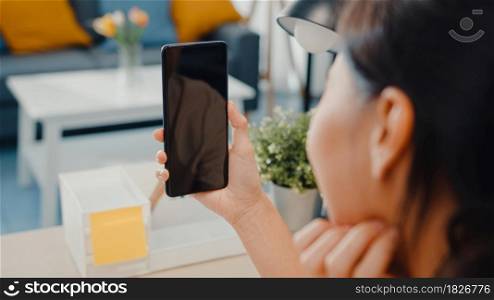 Young Asia lady use smart phone with blank black screen mock up display for advertising text while smart working from home at living room. Chroma key technology, Marketing design concept.