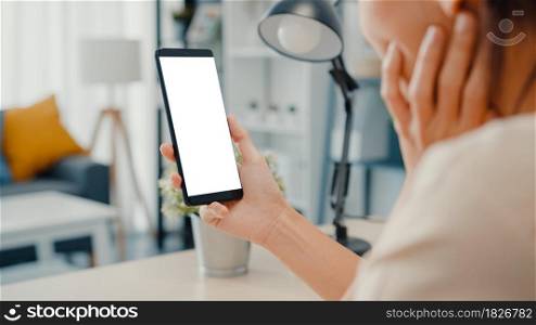 Young Asia lady use smart phone with blank white screen mock up display for advertising text while smart working from home at living room. Chroma key technology, Marketing design concept.