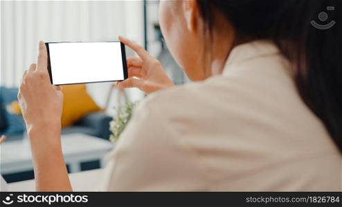 Young Asia lady use smart phone with blank white screen mock up display for advertising text while smart working from home at living room. Chroma key technology, Marketing design concept.
