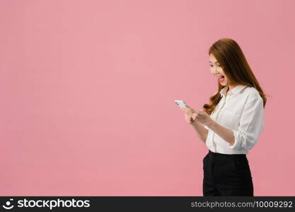 Young Asia lady using phone with positive expression, smiles broadly, dressed in casual clothing feeling happiness and standing isolated on pink background. Happy adorable glad woman rejoices success.