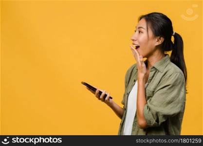 Young Asia lady using phone with positive expression, smiles broadly, dressed in casual clothing feeling happiness and stand isolated on yellow background. Happy adorable glad woman rejoices success.