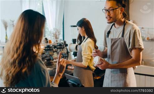 Young Asia male barista waiter taking order from customer standing behind bar counter while talking with customer making note on takeaway coffee cup at cafe restaurant. Owner small business concept.