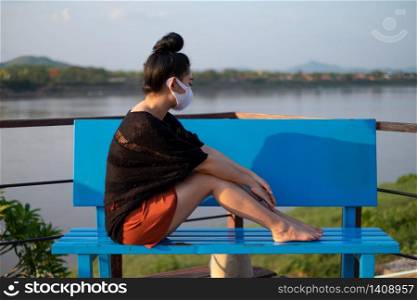 Young Asia woman sitting at the blue bench and putting on a medical mask to protect from airborne respiratory diseases as the flu dust and smog in the park, Women safety virus infection concept
