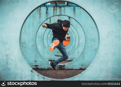 Young Asian active man jumping and kicking action, circle looping wall background. Extreme sport activity, parkour outdoor free running, or healthy lifestyle concept
