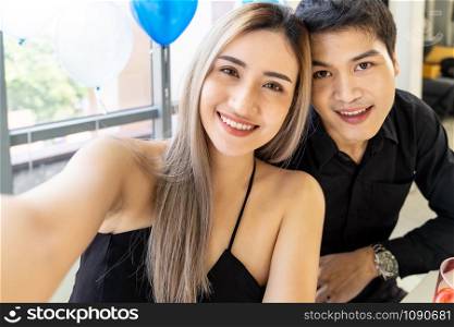 Young asian adult couple make selfie photographing for celebrateing New Year and Christmas holiday together in living room of big apartment in big city.