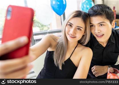 Young asian adult couple make selfie photographing for celebrating New Year and Christmas holiday together in living room of big apartment in big city.