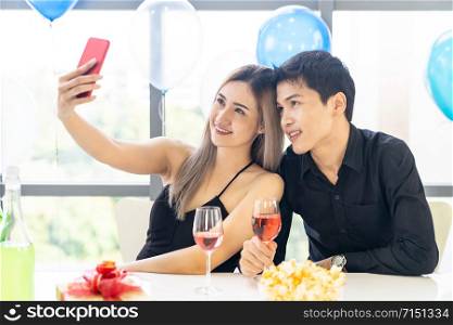 Young asian adult couple make selfie photographing for celebrating New Year and Christmas holiday together in living room of big apartment in big city.