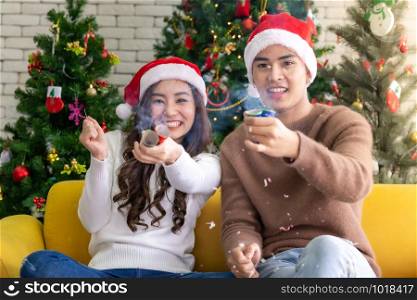 Young asian adult teenager couple celebrateing christmas holiday together with Firecrackers in living room with christmas tree decoration.