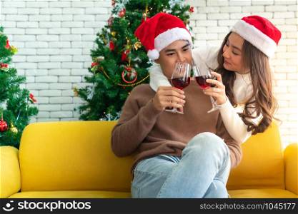 Young asian adult teenager couple celebrateing christmas holiday with wine together in living room with christmas tree decoration.