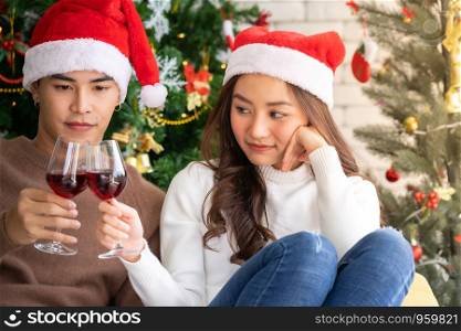 Young asian adult teenager couple celebrateing christmas holiday with wine together in living room with christmas tree decoration.
