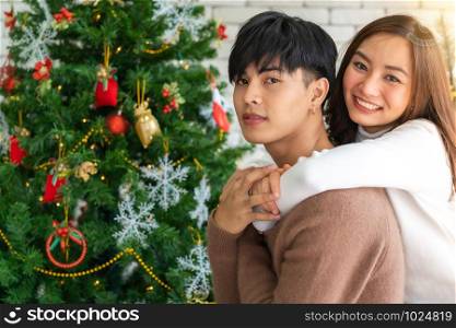 Young asian adult teenager couple hugging and celebrateing christmas holiday together in living room with christmas tree ornament decoration.
