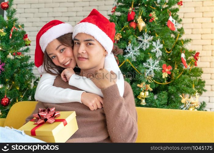 Young asian adult teenager couple hugging and celebrateing christmas holiday together in living room with christmas tree decoration.