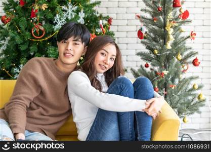 Young asian adult teenager couple hugging and celebrateing christmas holiday together in living room with christmas tree decoration.