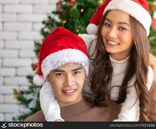 Young asian adult teenager couple hugging and celebrateing christmas holiday together in living room with christmas tree decoration.